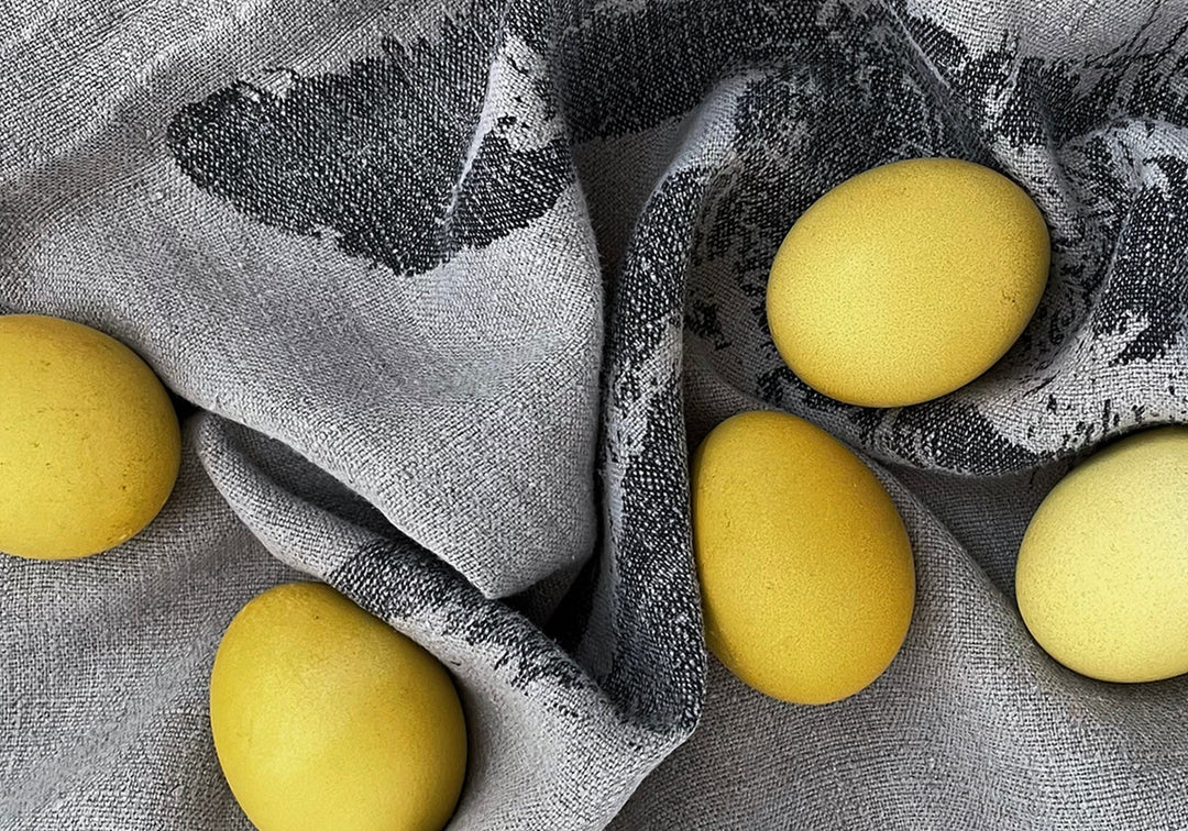 Du siehst ein bedrucktes Geschirrtuch, darauf liegen fünf mit getrockneter Kamille gefärbte (Oster) Eier.